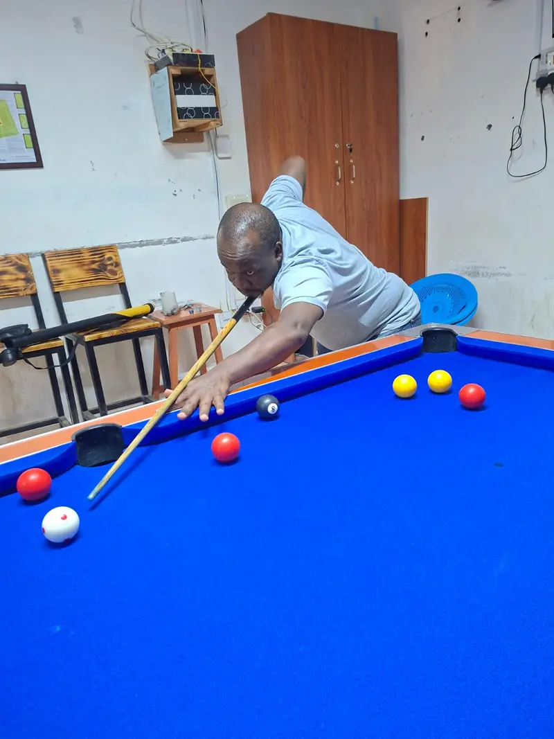 A player stretches across a blue pool table to reach the cue ball for a long shot.